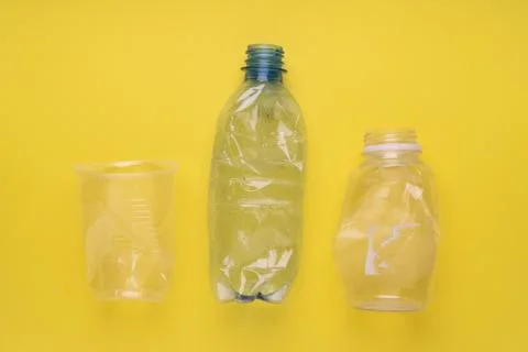 Crashed plastic bottles and a cup on yellow background. Plastic utilisation Stock Photos
