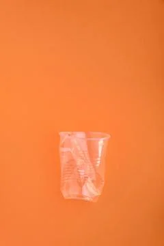 Crashed plastic cup on orange background. Plastic utilisation concept Stock Photos