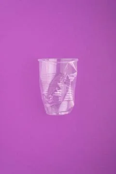 Crashed plastic cup on purple background. Plastic utilisation concept Stock Photos