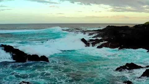 Crashing ocean waves against rugged black rocks under a cloudy sky dramatic Stock Footage 344241499