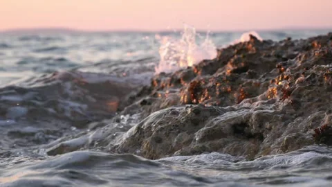 Crashing ocean waves splash over wet rocks at golden sunset Stock Footage 337305574
