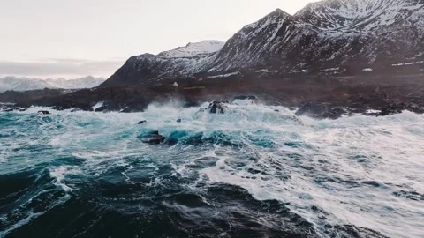 The Crashing Waves Collide Powerfully Against the SnowCovered Mountains in the Stock Footage 303704822