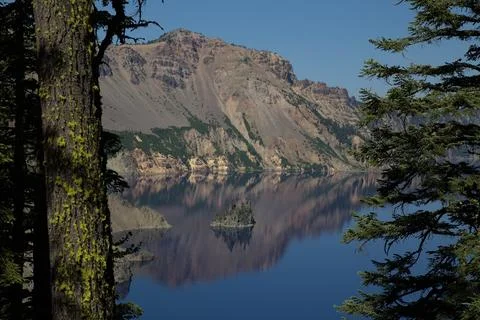 Crater Lake mirror reflection of rugged mountain cliffs framed by pine tree.. Stock-Fotos