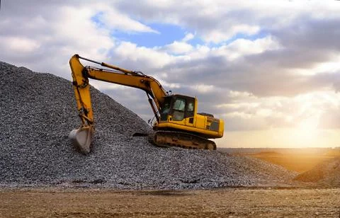 Crawler excavator in the rays of the setting sun at sunset digs earth and san Stock Photos