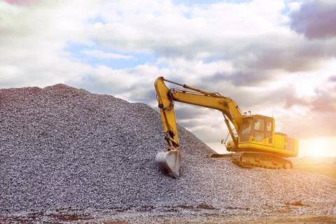 Crawler excavator in the rays of the setting sun at sunset digs earth and san Stock Photos