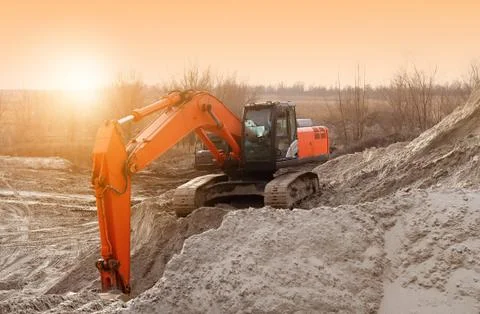 Crawler excavator in the rays of the setting sun at sunset digs earth and san Stock Photos