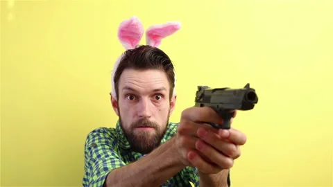 Crazy bearded man in bunny ears with toy gun in hands on yellow background Stock Footage 148226623