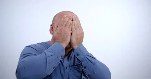 Crazy drunk bald man in a blue shirt makes a face covering his face with his Stock Footage 119338467