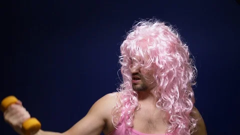 Crazy guy athlete in a wig with dumbbells against a dark background Stock Footage 117071187