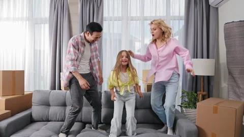 Crazy kid jump sofa. Happy people buy real estate. Fun family move new apartment Stock Footage 253401501