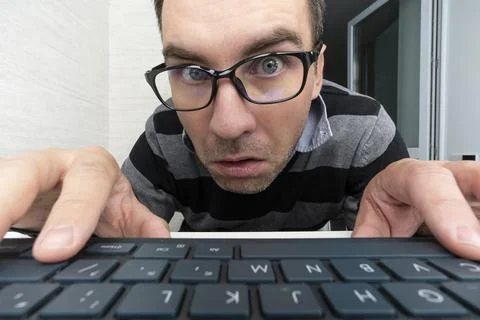 Crazy looking man typing on the keyboard and looks at camera. Surprised man a Stock Photos