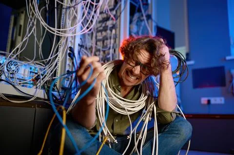 Crazy mad computer engineer wrapped in wires and cables in server room Stockfoto's