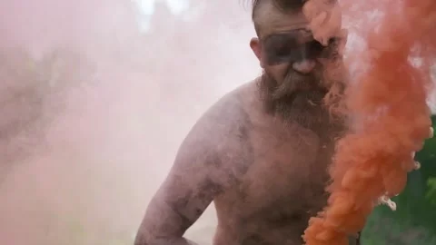Crazy man with no clothes, stern eyes, walking through smoke, looking at camera Stock Footage 131379142