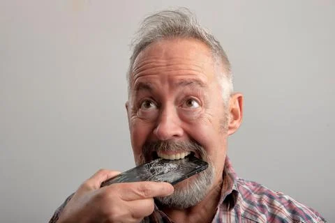 Crazy Middle age grey-haired man eats his smartphone Stock Photos