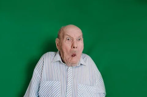 A crazy old man makes faces and grimaces against an isolated green background Stock Photos