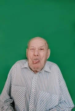 A crazy old man makes faces and grimaces against an isolated green background 写真素材