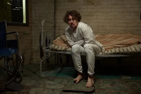 Crazy psycho man wearing straitjacket sitting on hospital bed Stock Photos