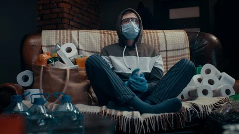 Crazy scared man spraying antiseptics around sitting on sofa in front of TV 動画素材 126665837