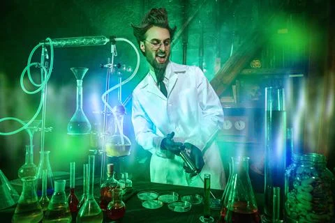 Crazy scientist works in his laboratory, lit by a mysterious green light. Cha Stock Photos