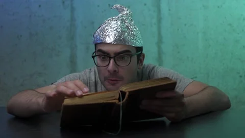 Crazy Tin Foil Hat Man Reading a Book To Get Informations Stock Footage 136132545