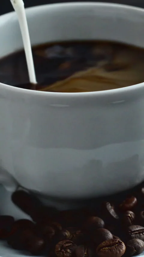 Cream is poured into a cup of espresso coffee and coffee beans. Video stock 253233144