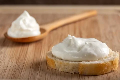 Creamy fresh cheese spread on rustic bread with wooden spoon. Stock Photos