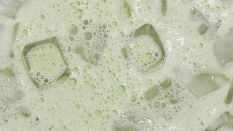 Creamy matcha tea with ice cubes and airy foam bubbles, top view macro reveals Stock Footage 318285714