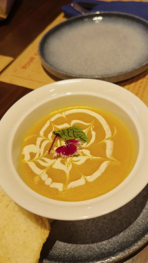 Creamy pumpkin soup serving in a white bowl with decorative cream art and fresh Stock Footage 344911070