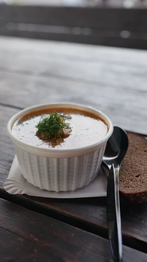 Creamy soup served in white ramekin with fresh dill garnish, spoon, and rye 스톡 동영상 344770182
