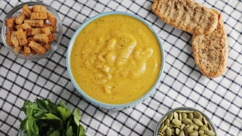 Creamy vegetable soup with bread, seed pumpkin, herbs, rusks. Table served with Video stock 330537483