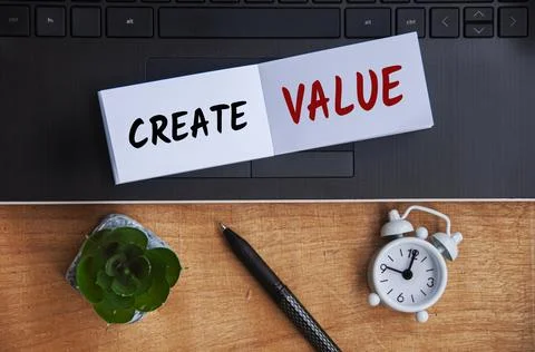 Create value text on notepad with laptop, clock, pen and wooden background. B Stock Photos