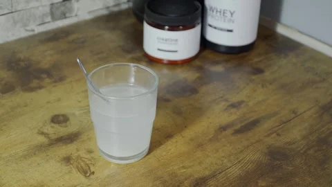 Creatine dissolving in water with whey protein beside Video stock 313564678
