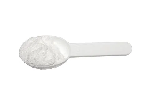 Creatine in a measuring plastic spoon on a white background. Stock Photos
