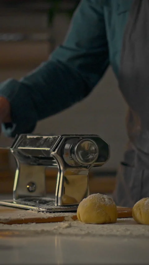 Creating fresh pasta using a manual pasta machine in a cozy kitchen setting Stock Footage 331541328