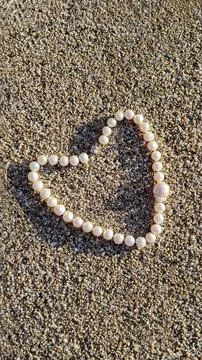 Creating a heart shape on sand using small round beads to express love in a.. Foto stock