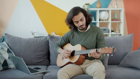 Creative Arab man playing the guitar and using laptop watching tutorial at home 库存影片 135251974