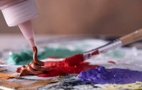 Creative artist using paintbrush to mix green and red oil paint on colorful p Stock Photos
