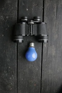 Creative background with binoculars and blue light bulb Stock Photos