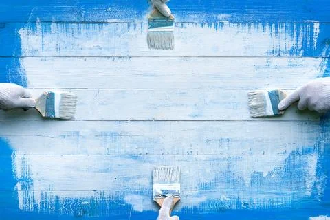 Creative background with four hands painting blue wooden boards with white .. Stock Photos
