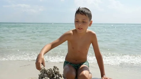 A creative boy builds a sandy castle on a sea shore on a sunny day in slo-mo Stock-Footage 81437770