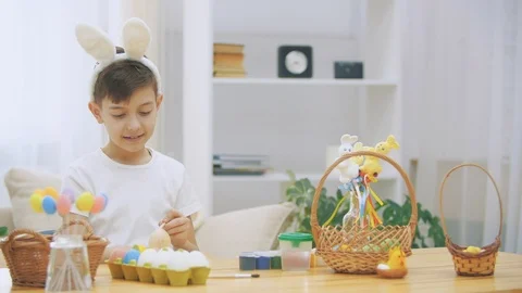 Creative boy is colorizing an Easter egg with a help of paint-brush., wearing Stock Footage 104636726