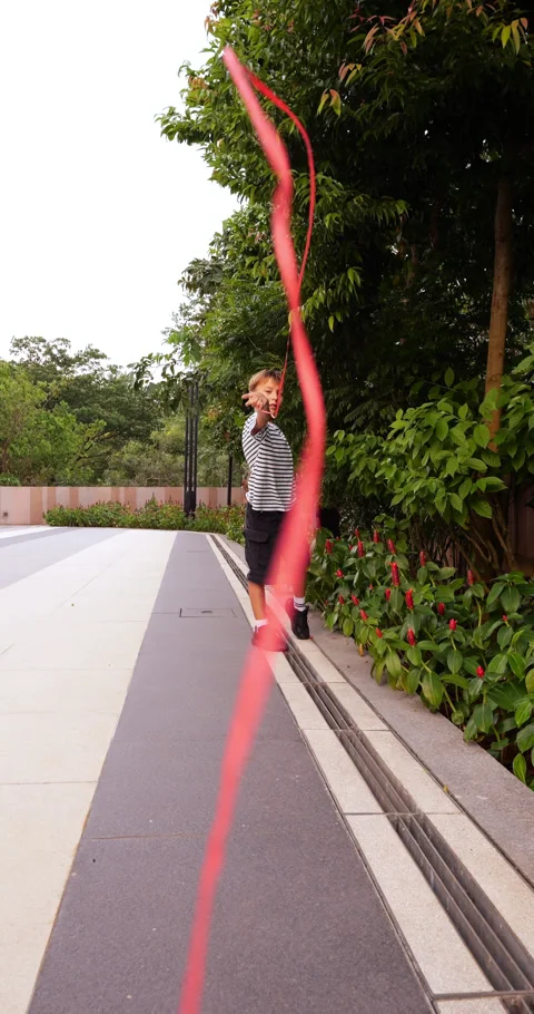 Creative boy playing with red ribbon flying from his arm, slow motion shot Stock Footage 304160230
