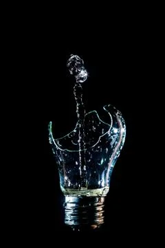 Creative broken light bulb with water fountain on isolated black background w Stock Photos