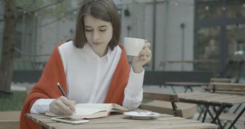 Creative brunette writer is taking notes in her notebook and drinking coffee on Stock Photos