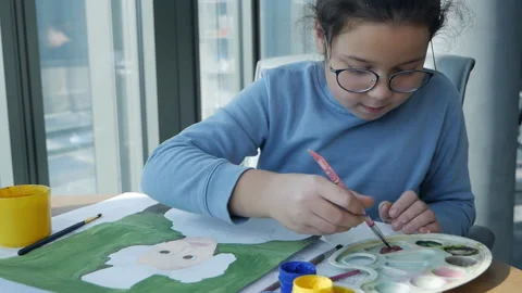 Creative child learns to draw on paper. A little girl sitting at the table draws 스톡 동영상 163652620