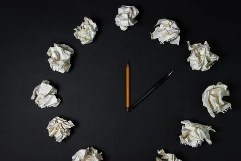 Creative clock on a black background. A clock of crumpled paper and a pen with a Stock Photos