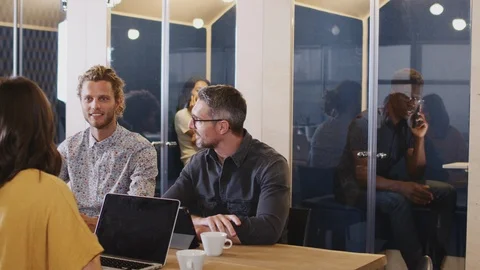 Creative colleagues sitting at table socialising in the office canteen, panning Stock Footage 111929128