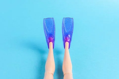 Creative composition with doll legs and flippers on blue background. Stock Photos