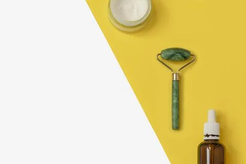 Creative composition with jade roller, face cream, serum on two color yellow and Fotos de archivo
