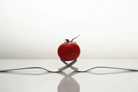 Creative composition of two forks and a red cherry tomato isolated on a white Stock Photos